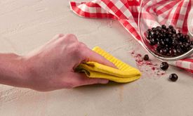 Hand wischt Beerenfleck mit gelbem Tuch weg