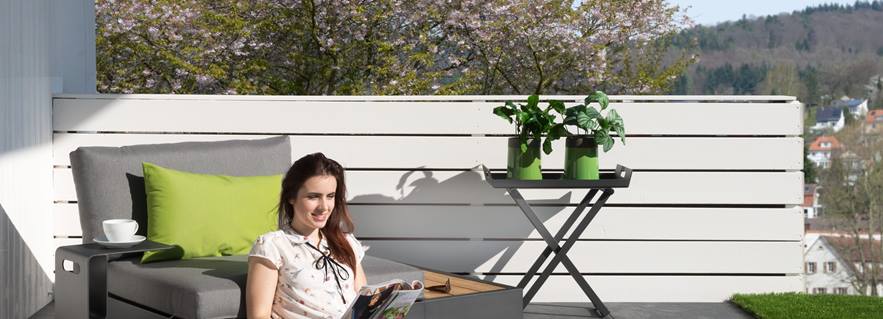 Frau sitzt auf Terrasse mit grauen Platten in Schieferoptik und modernen Möbeln
