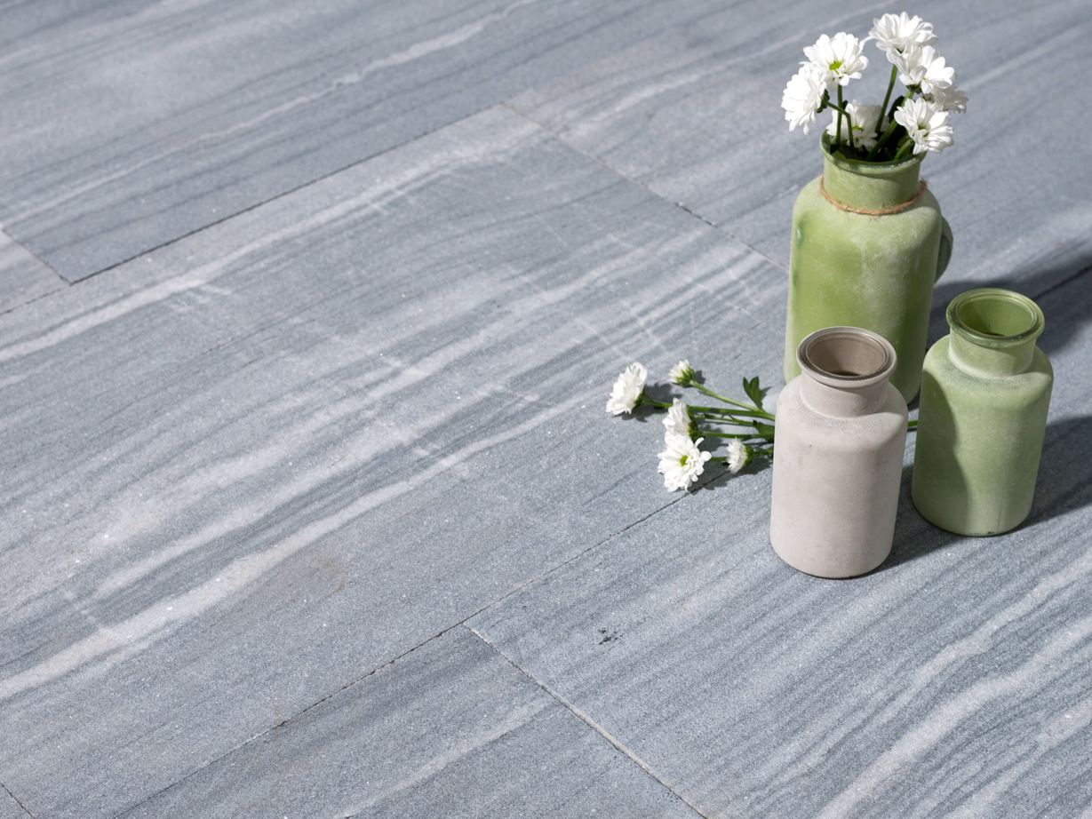 Facettenreiche Grautöne und feine Steinzeichnungen geben den Kalksteinplatten Ocean Grey den Look! Drei Vasen mit Blumen auf Kalksteinplatten in hellem Grau mit weißen Maserungen