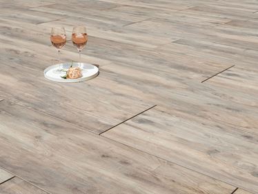 Zwei Weingläser und eine Blume auf Terrassenplatten in Holzoptik