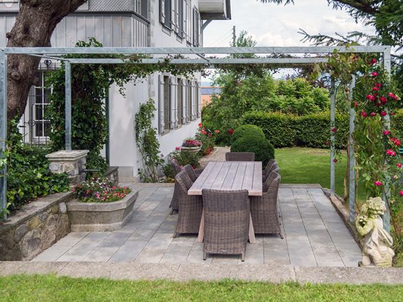 Naturstein in Grau: dezent und elegant Sandsteinplatte Kandla Grey auf einer Terrasse mit Pergola und angrenzendem Rasen