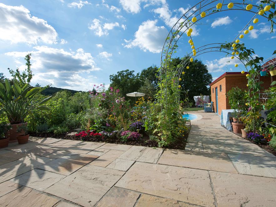 Helle Platten aus Sandstein Yellow Mint mit naturnahem, mediterranem Garten im Hintergrund