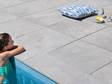Mädchen im Pool stützt sich mit Ellbogen an der Poolumrandung mit Schieferoptikplatten Alpine Grey ab.