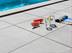 Melonen, Wasserglas, Wasserkaraffe und Zeitschrift liegen auf der Feinsteinzeug-Terrasse Alpine Grey mit Pool