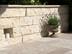 Natursteinmauer aus hellem Naturstein mit Pflanzenkübel davor und angrenzendem Natursteinboden aus Travertin