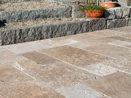 Terrasse mit Natursteinplatten aus braunem Travertin, im Hintergrund eine Treppe mit Granitsteinen