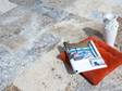 Rotes Kissen mit Zeitschrift und eine weiße Vase auf silbergrauen Natursteinplatten Travertin