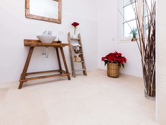 Badezimmer mit Holzmöbeln und hellen Natursteinfliesen aus Kalkstein als Bodenbelag