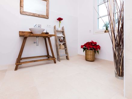 Badezimmer mit Holzmöbeln und hellen Natursteinfliesen aus Kalkstein als Bodenbelag