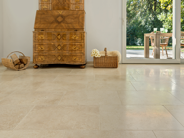 Antiker Holzschrank auf hellen Kalksteinfliesen Cleopatra Light, im Hintergrund Blick auf die Terrasse und den Garten