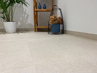 Nahaufnahme von Boden mit Feinsteinzeug-Fliesen Sevilla Cream in Kalksteinoptik. Im Hintergrund ein Holzregal, eine Pflanze und Deko