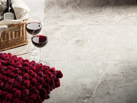 Zwei Weingläser stehen neben Korb mit Weinflasche und rotem Kissen auf Marmorfliesen Silver Shadow poliert