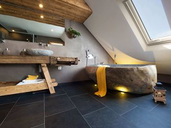 Rustikales Bad mit Badewanne in Steinoptik und dunklen Schieferfliesen als Bodenbelag