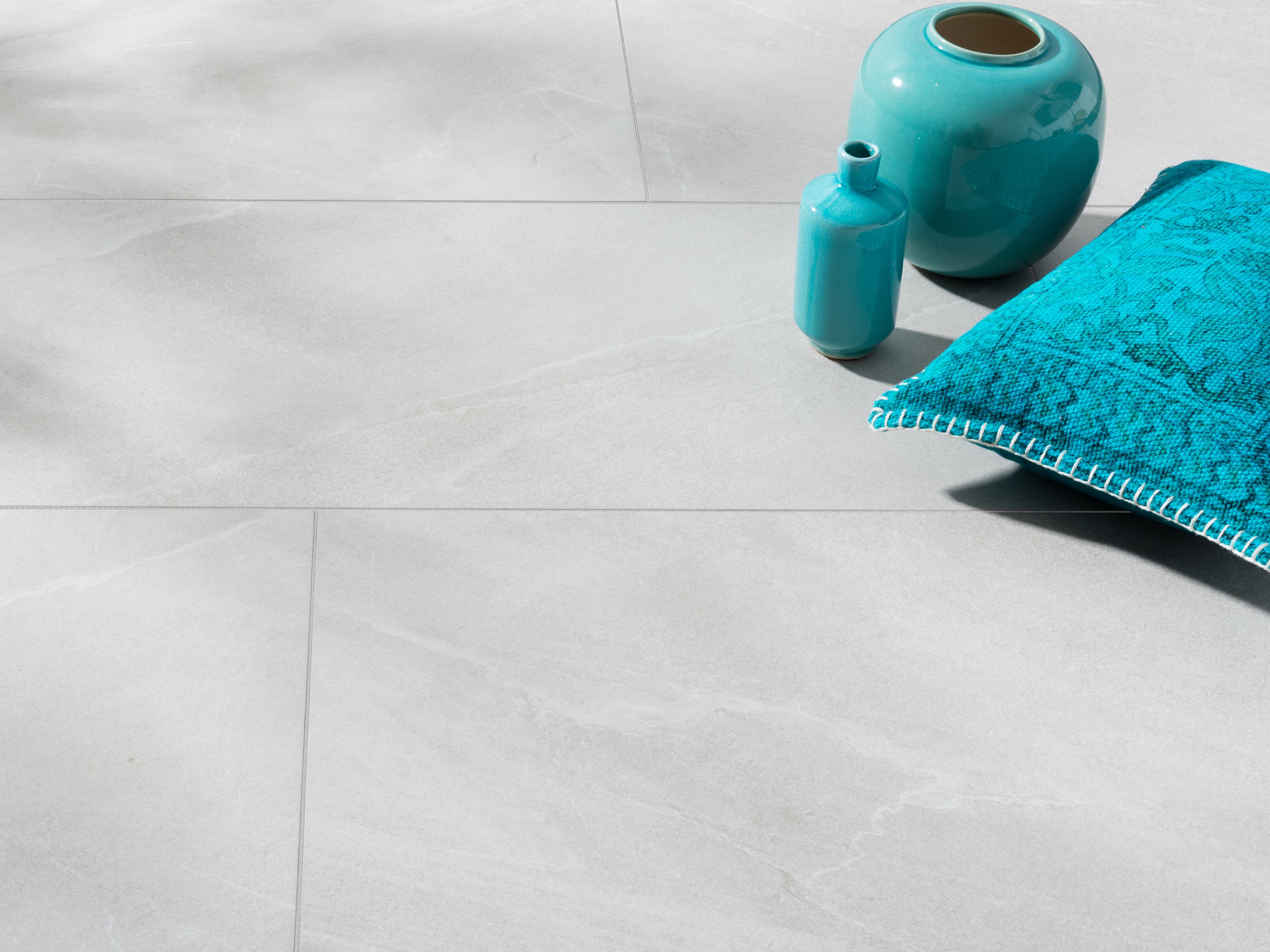 Feinsteinzeug-Fliesen in hellgrauer Schieferoptik mit türkiser Vase und türkisem Kissen