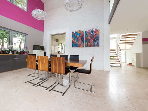 Offener Essbereich mit modernen Holzstühlen und buntem Gemälde an der Wand, Bodenbelag helle Travertinfliesen mit geschliffener Oberfläche