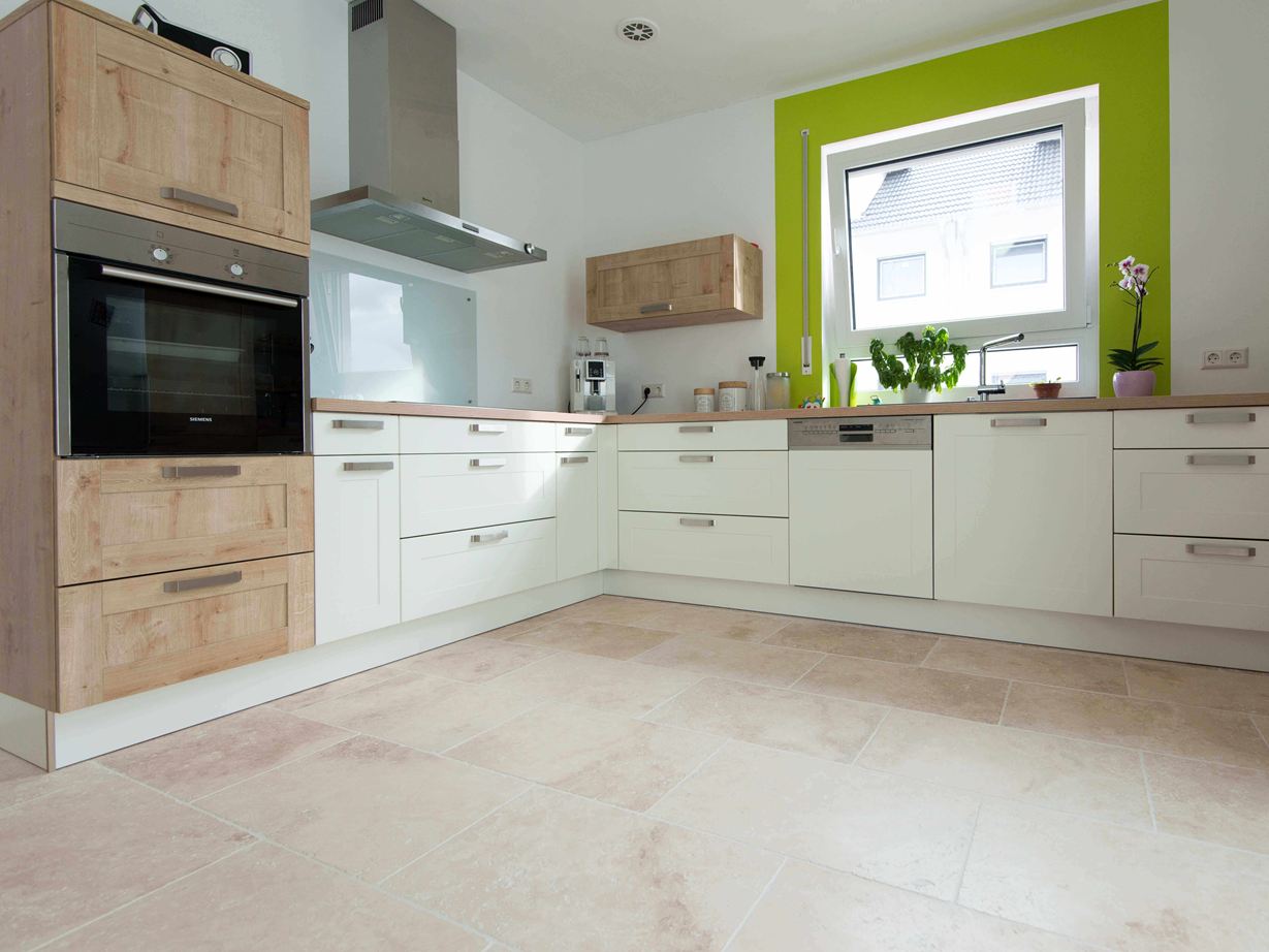 Travertin Light: Moderne Wirkung und Format Küche in Weiss mit Holzelementen und grüner Fensterumrahmung auf Travertinfliese Light mit getrommelter, ungespachtelter Oberfläche