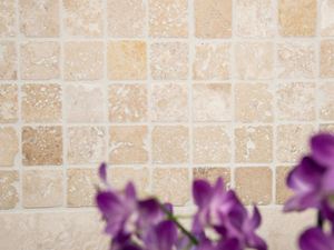 Lila Blüten vor einem beige-braunen Travertin-Mosaik
