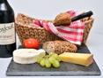 Brotkorb, Käse und Trauben auf einer Schieferplatte, daneben eine Weinflasche