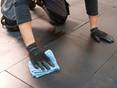 Verleger wischt verlegte Natursteinfliesen aus Schiefer mit einem blauen Tuch ab