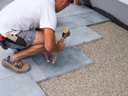 Verleger klopft Blausteinplatten mit einem Gummihammer im Edelsplittbett fest