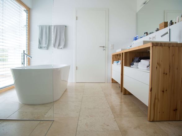 Bad mit freistehender Badewanne links und Waschtisch aus Holz recht, Travertinfliesen als Bodenbelag