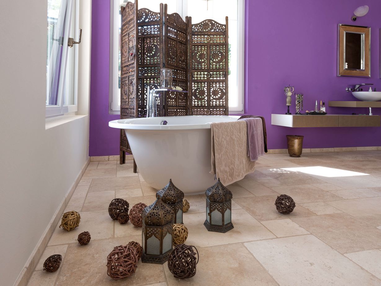 Fliesen aus Travertin Light in einem Bad mit freistehender Badewanne und lila Wand im Hintergrund