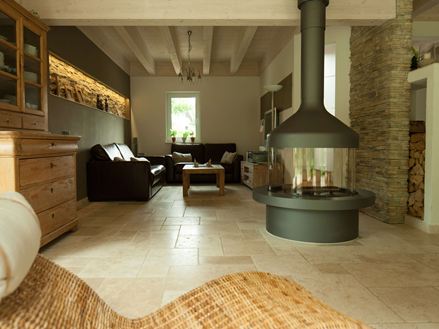 Wohzimmer mit alleinstehendem Kamin und Sitzecke auf Travertinfliese Light, im Vordergrund ein Korbsessel