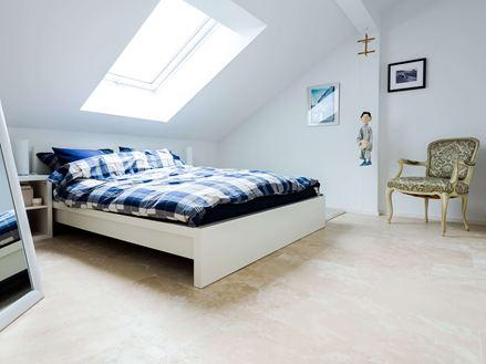 Ein helles Schlafzimmer unter dem Dach mit Travertinfliesen Medium Line als Bodenbelag