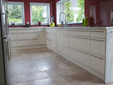 Kundenfoto einer Küche mit weißen Möbeln, roten Wänden und beige-braunen Travertinfliesen