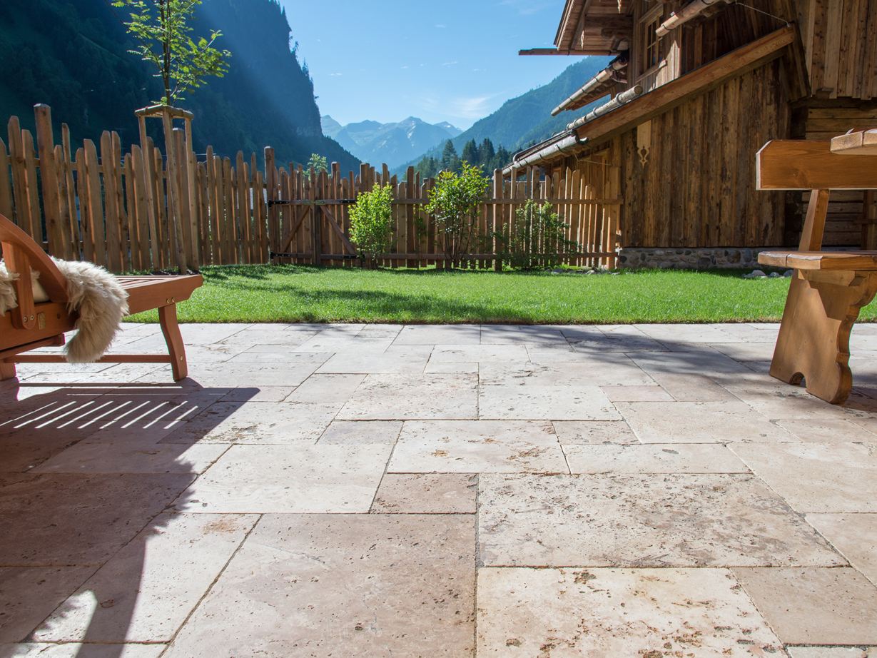 Terrassenboden mit Travertin Rustic und Holzmöbeln, im Hintergrund eine Rasenfläche und Ausblick auf die Berge