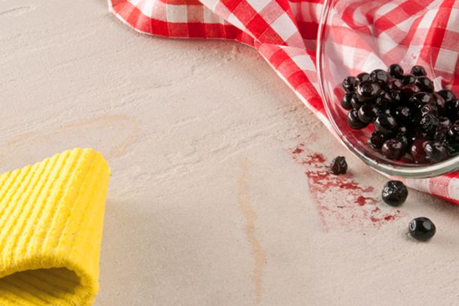 Gelber Lappen, rotes Geschirrtuch und eine Glasschale mit ausgekippten Beeren auf Naturstein