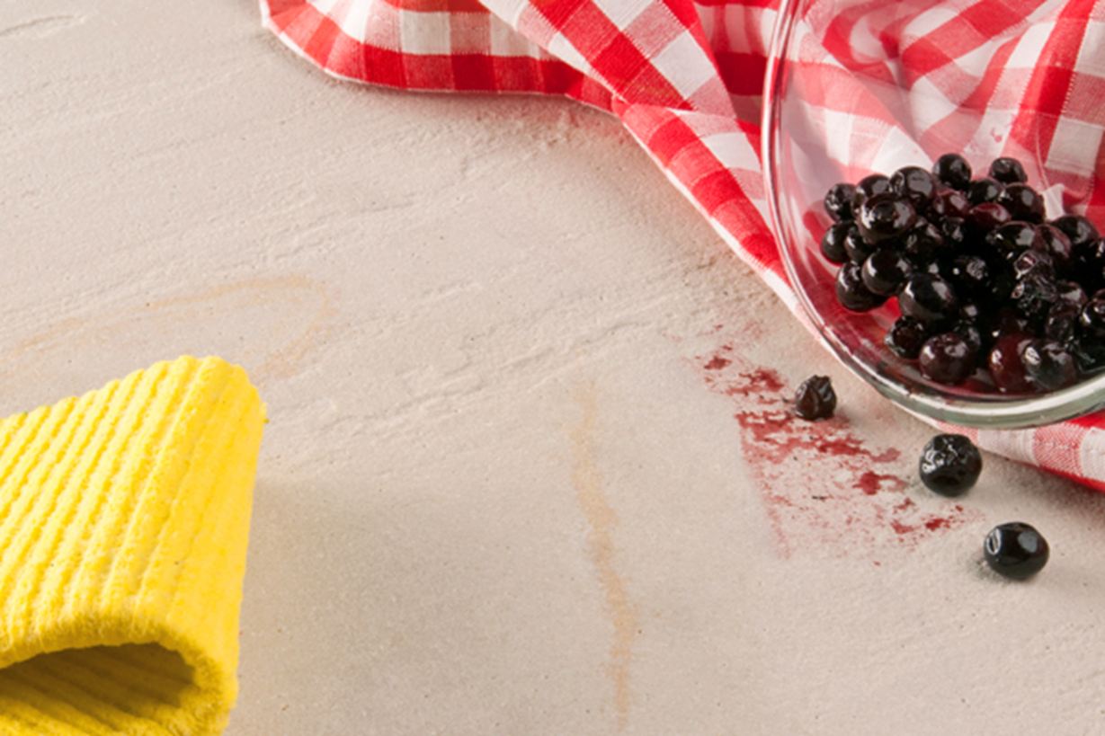 Gelber Lappen, rotes Geschirrtuch und eine Glasschale mit ausgekippten Beeren auf Naturstein
