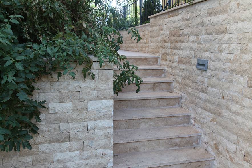 Mauersteine aus Naturstein mit natursteinverkleideter Treppe und Pflanzen in der linken Bildhälfte