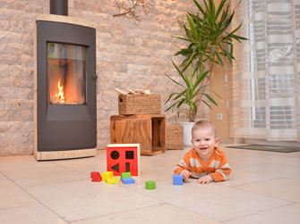 Baby spielt auf Natursteinboden vor einem Kamin