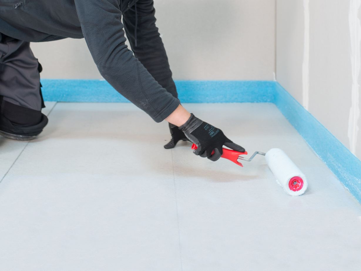 Fliesenleger bringt die Grundierung mit einer Rolle auf