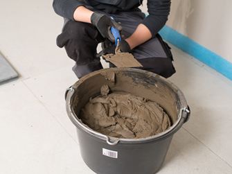 Fliesenleger vor einem Eimer mit Natursteinkleber