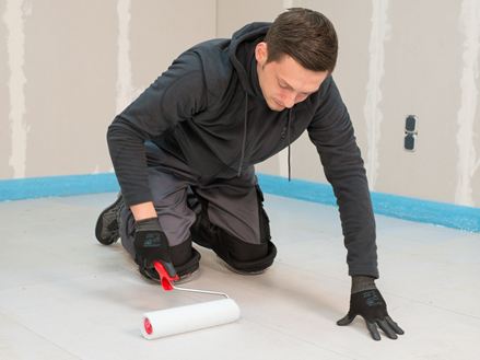 Fliesenleger trägt die Grundierung mit einer Walze auf