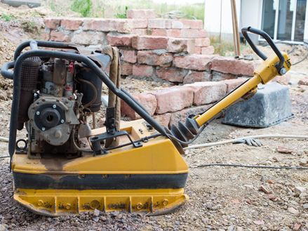 Foto einer Rüttelplatte auf einer Baustelle, die zur Verdichtung der Schottertragschicht verwendet wird