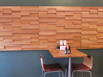 Ein Tisch mit zwei Stühlen vor einer grauen Wand mit braunen Holzverblendern in einem Bistro