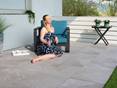 Feinsteinzeug in hellgrau: Diese Terrassenplatten sind ideal für Sonnenbäder auf der Terrasse! Frau sitzt auf sonniger Terrasse mit Schieferoptikplatten Alpine Grey