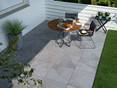 Die Terrassenplatten Alpine Grey kommen mit modernen Möbeln besonders gut zur Geltung. Frühstückstisch auf einer Terrasse mit modernen Feinsteinzeugplatten in Schieferoptik
