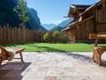 Ein Traum: Einzigartiger Ausblick von der Travertinterrasse auf die Berglandschaft Terrassenboden mit Travertin Rustic und Holzmöbeln, im Hintergrund eine Rasenfläche und Ausblick auf die Berge