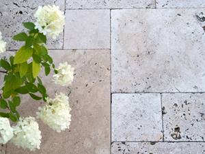 Getrommelte Oberflächen: rustikal und natürlich Beige Travertinplatten im Römischen Verband verlegt mit weißen Blumen von oben