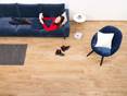 Frau liegt auf blauer Couch in einem Wohnzimmer mit Fliesen in Holzoptik Urban Honey, daneben ein Sessel mit weißem Kissen