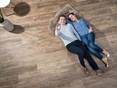 Diese Feinsteinzeug-Holzoptik verleiht Charme und Natürlichkeit. Paar liegt auf Holzoptikfliesen Indie Nova von oben fotografiert