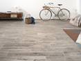 Die Feinsteinfliesen Urban Smoke passen zu einem vintage und trendigen-chic Look. Großzügiges Wohnzimmer mit Feinsteinzeug Urban Smoke als Bodenbelag, im Hintergrund lehnt ein Fahrrad an der weißen Wand